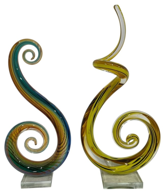ART GLASS SWIRL SCULPTURES PAIR 17": This pair of contemporary art glass sculptures features elegant freeform spiral designs in complementary color palettes. One sculpture showcases vibrant yellow, amber, and clear glass with black ribbo