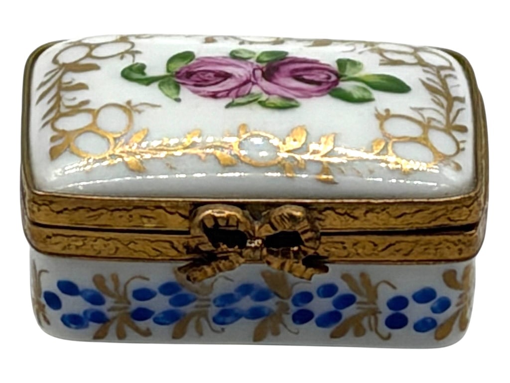 LIMOGES ELEGANT ROSE TRINKET BOX 1.5": Hand-painted Limoges porcelain rectangular trinket box featuring two elegant pink roses framed by elaborate gilt foliate decoration. Finished with ornate brass-tone mounts and a decorative bow clasp, 