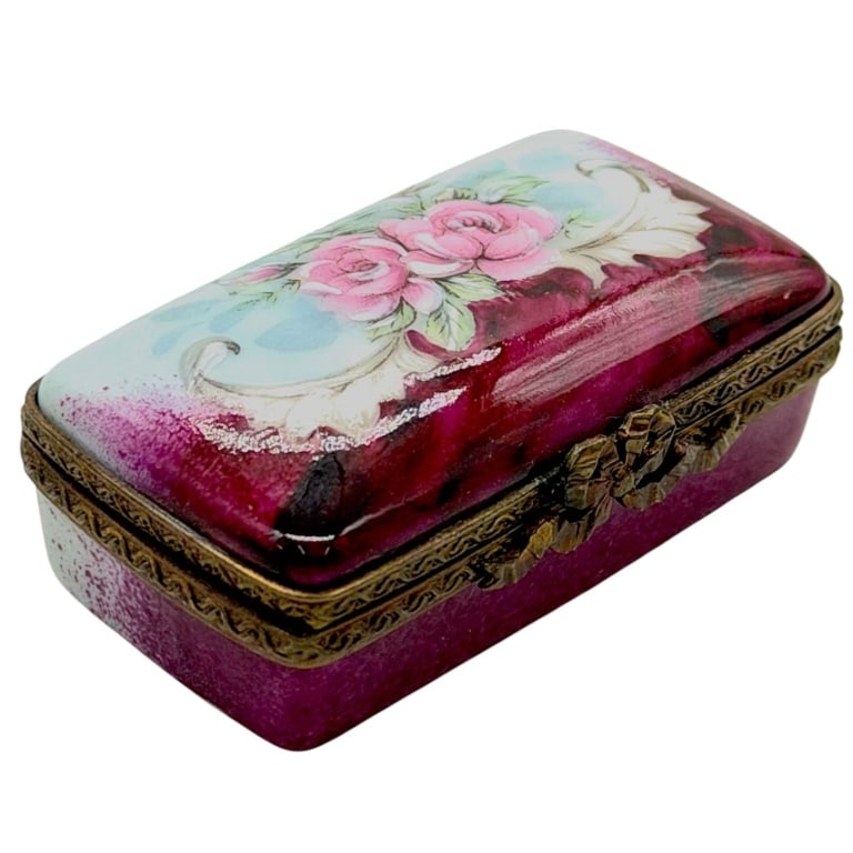 LIMOGES RED ROSE PORCELAIN BOX 2": Beautiful hand-painted Limoges porcelain rectangular trinket box decorated with pink roses against a rich burgundy and pale blue background with scrolling white accents. Finished with ornate brass-ton