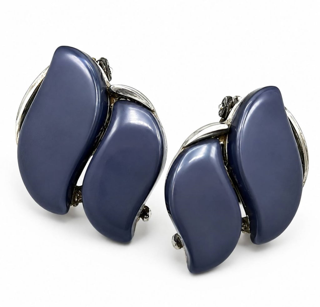 VINTAGE LISNER BLUE LUCITE CLIP-ON EARRINGS 1": Vintage Lisner clip-on earrings featuring sculptural navy blue Lucite panels gracefully set within silvertone frames. The abstract leaf-inspired design reflects the clean, modern styling popular durin