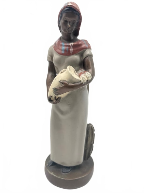 Native American Woman Ceramic Figurine: Ceramic figurine depicting a Native American woman in traditional attire, holding a pottery vessel. Features a long dress, headscarf with a geometric pattern, and a cactus detail at the base. Height i