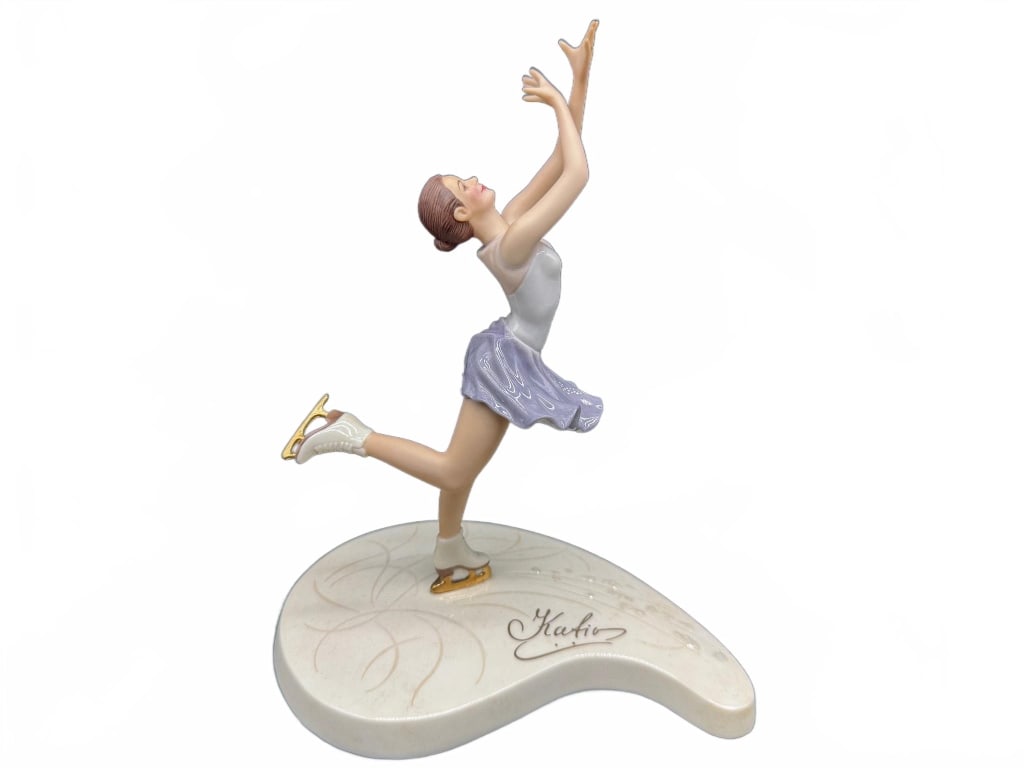 Kim Anderson Ice Skater Figurine: Kim Anderson's Celebration of Life porcelain figurine depicting a female ice skater in a lavender skirt and white top, mounted on a signature base. Marked on the underside, approximately 8.5 inches ta