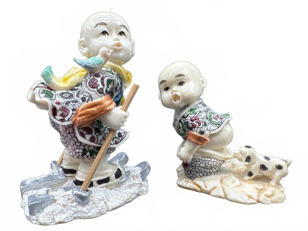 Porcelain Chinese Boy Figurines: Hand-painted porcelain figurines featuring young Chinese boys in traditional clothing, one with a bird and shovel, the other with a spotted dog. Each shows floral and mark detailing on the base.