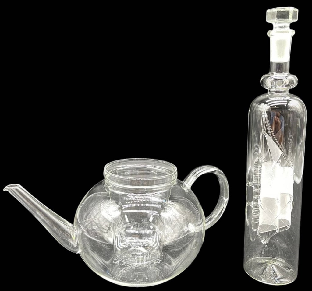 GLASS TEAPOT & SHIP DECANTER LOT 11": Collection of two decorative clear glass pieces including a contemporary glass teapot with integrated infuser and a tall etched ship decanter with matching stopper. The teapot features a rounded body,