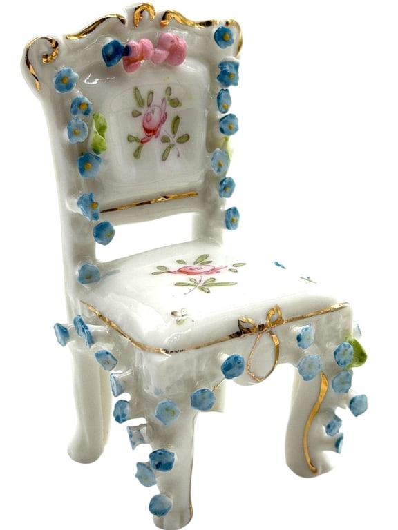 PORCELAIN FLORAL MINIATURE CHAIR 4": This decorative porcelain miniature is modeled as an ornate side chair with a shaped Rococo-style back, cabriole legs, and molded apron. The white glazed body is hand-painted with pink rose sprays and