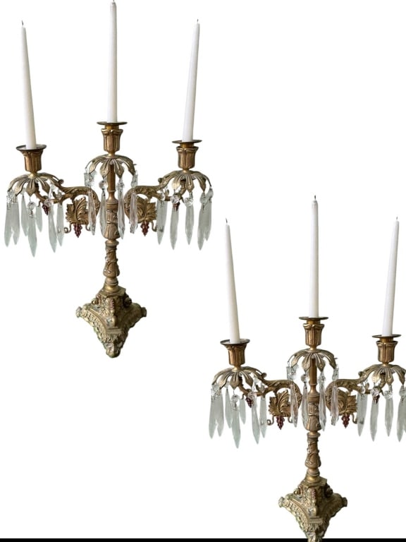 ANTIQUE BRASS SCONCES WITH PRISMS: Pair of antique brass wall sconces, each with three candle holders and adorned with hanging crystal prisms. Elegant ornate designs on the brass bases add to their vintage charm. Approximate height is 