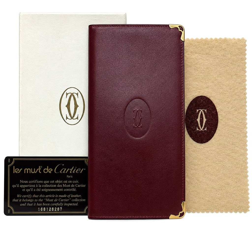 CARTIER VINTAGE BORDEAUX LEATHER LONG WALLET 7.5": A vintage Must de Cartier long wallet crafted in the maison's iconic Bordeaux leather with elegant gold-tone corner hardware and the signature embossed Double C logo. The interior offers multiple card