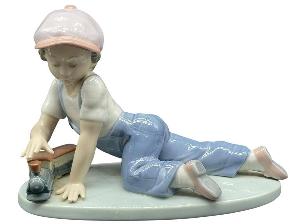 -LLADRO ?ALL ABOARD? #7619 PORCELAIN FIGURINE ? BO: -LLADRO “ALL ABOARD” #7619 PORCELAIN FIGURINE – BOY WITH TRAIN | | | -Charming Lladró porcelain figurine titled All Aboard (#7619), featuring a young boy playfully lying on his stomach as h