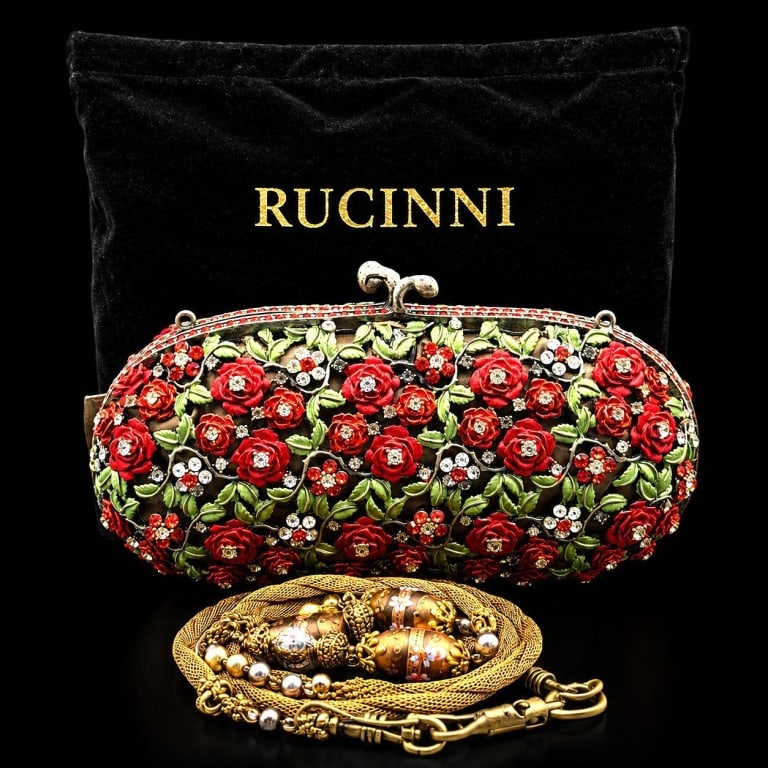 RUCINNI FLORAL CRYSTAL CLUTCH 6": This elegant Rucinni hard-sided minaudi?re showcases a lush garden of sculpted crimson roses intertwined with green enamel leaves and brilliant clear and ruby-colored crystals across the entire exteri