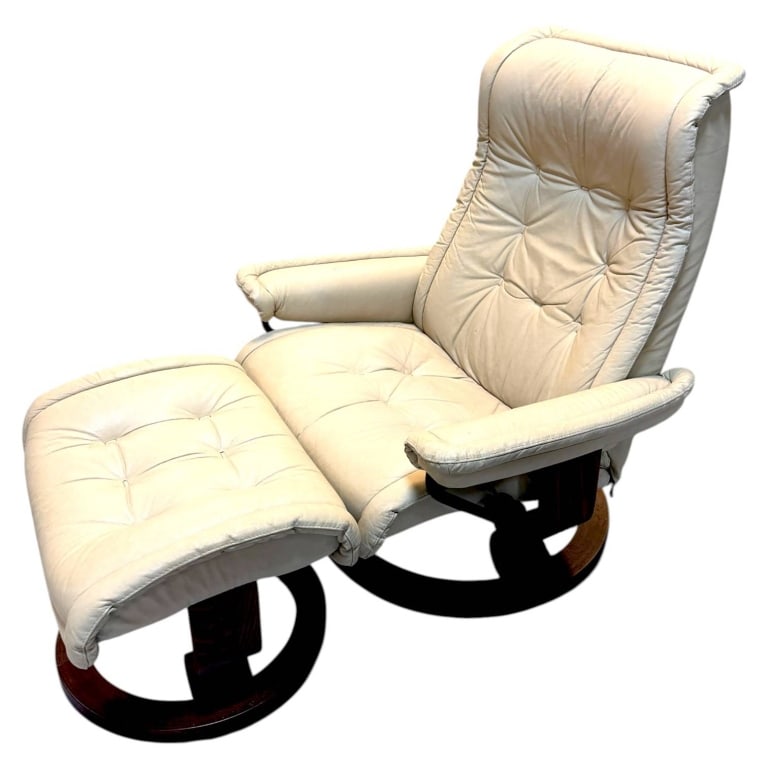 EKORNES STRESSLESS LEATHER RECLINER 40": Ekornes Stressless-style lounge chair with coordinating ottoman, upholstered in soft ivory leather over sculpted dark-stained wood circular bases. The high-back recliner features deep button-tufted cu