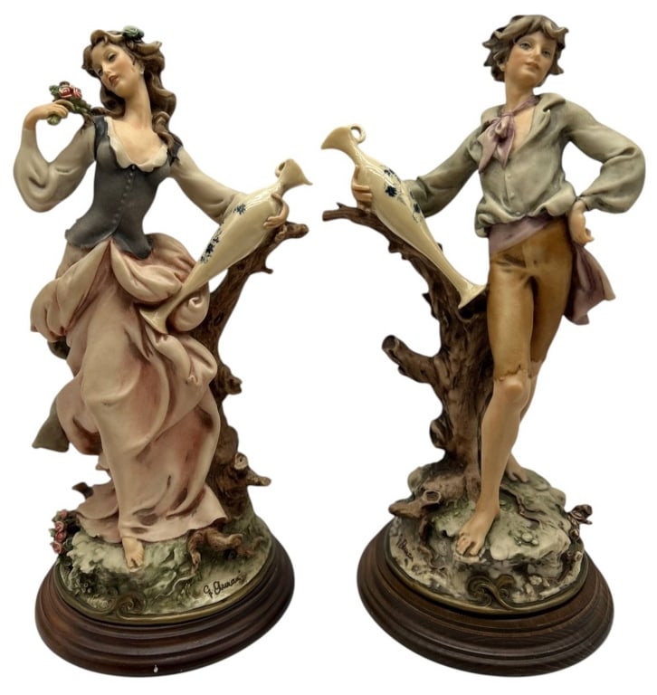 PAIR OF G. ARMANI FIGURAL SCULPTURES 14": Elegant pair of G. Armani by Florence porcelain figurines depicting a graceful young woman and gentleman, each posed beside a rustic tree branch supporting a decorative amphora. Beautifully hand-paint