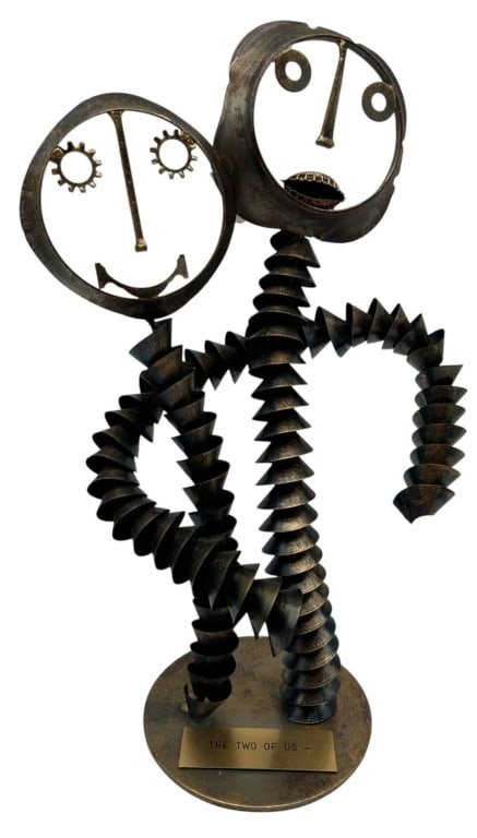 THE TWO OF US METAL SCULPTURE 13": Whimsical modern metal sculpture titled "The Two of Us", depicting two abstract human figures with expressive geometric faces and accordion-style spiral bodies. The handcrafted design features cut-met