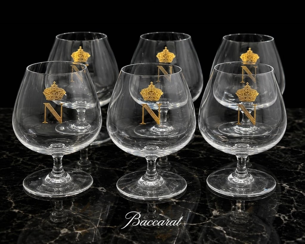 BACCARAT NAPOLEON COGNAC GLASSES 6PC SET 6": A sophisticated set of six Baccarat crystal cognac snifters, each elegantly decorated with a gold Napoleonic "N" beneath an imperial crown. These generously proportioned balloon bowls are designed to 