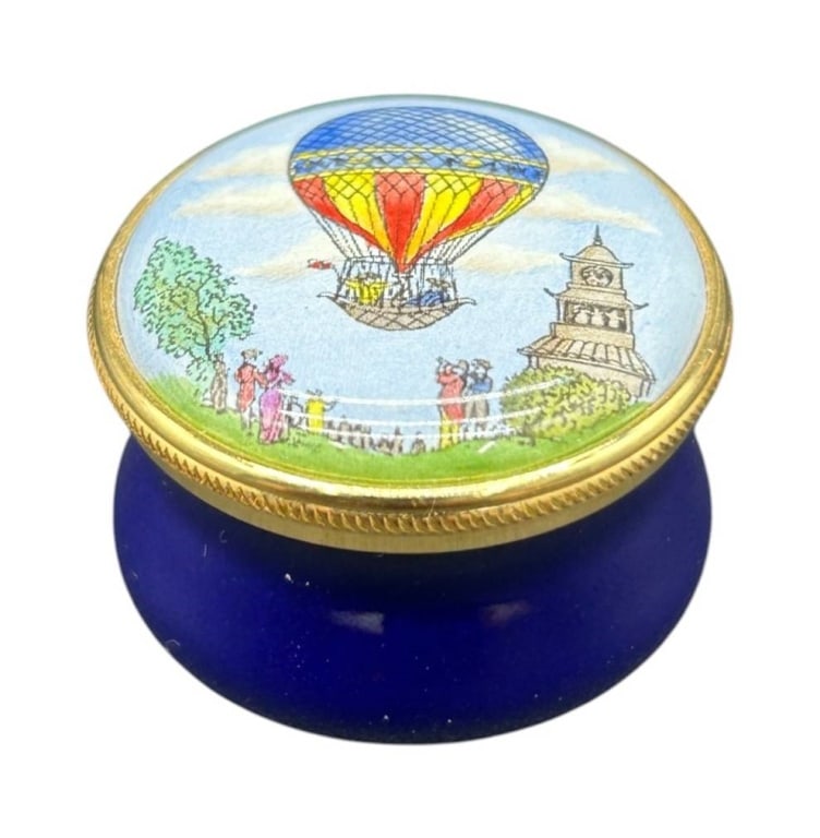 STAFFORDSHIRE ENAMELS HOT AIR BALLOON BOX 1": Hand-painted Staffordshire Enamels collectible trinket box featuring a colorful hot air balloon scene with figures and architectural details. Crafted in England, this petite enamel box has a rich coba