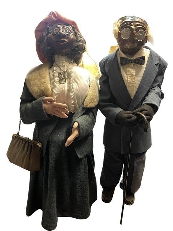 ELDERLY COUPLE DOLLS IN CLOTHING 44": Pair of elderly couple dolls, each dressed in period-style fabric clothing. Details include eyeglasses, jewelry, and accessories such as a cane and handbag. The dolls are crafted with expressive faces