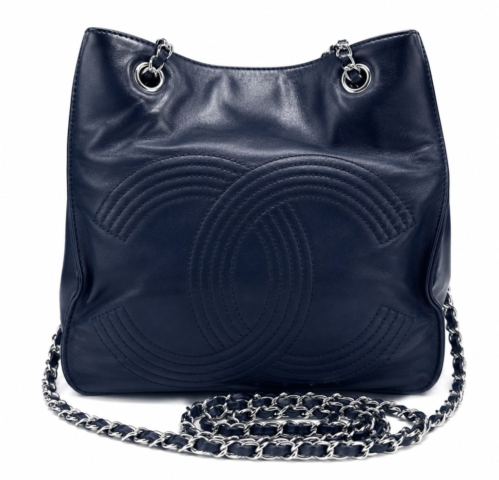 CHANEL NAVY LEATHER CC W SILVER BUCKET 9": Supple navy leather Chanel tote handbag featuring oversized stitched interlocking CC logo detailing across the front, silver-tone chain and leather shoulder straps, and a spacious open-top silhouette.