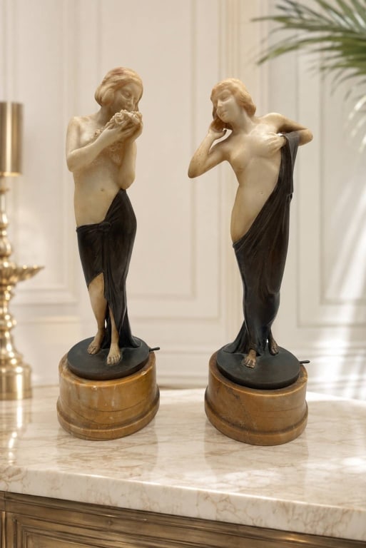 PAIR MARBLE & BRONZE ART DECO FEMALE SCULPTURE 14": Pair of Art Deco female figural sculptures, each modeled in an elegant classical pose with contrasting ivory-tone bodies and dark flowing drapery. One figure holds a floral bouquet while the