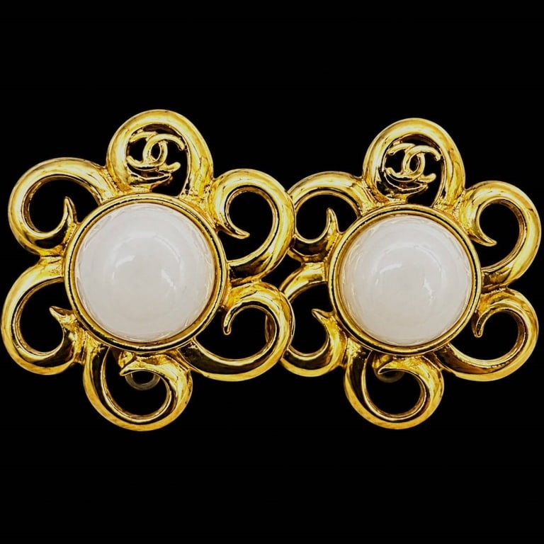 CHANEL VINTAGE GRIPOIX FLOWER CLIP EARRINGS 1.5": Vintage Chanel gold-tone clip-on earrings featuring bold openwork scrolling motifs surrounding large domed white cabochon centers. Each earring incorporates the iconic interlocking CC logo within the 