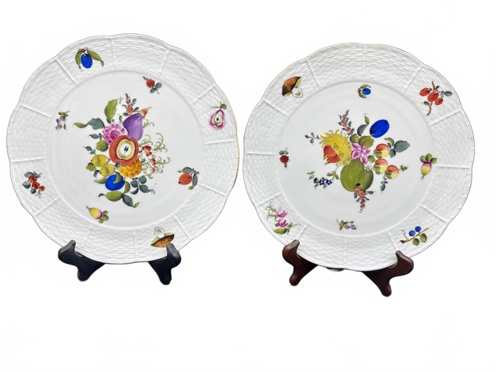 Herend Hand-Painted Porcelain Plates: Two Herend porcelain plates, each finely hand-painted with vibrant floral and fruit designs. The plates feature textured, basketweave-style borders and colorful decorative motifs, typical of Herend cr