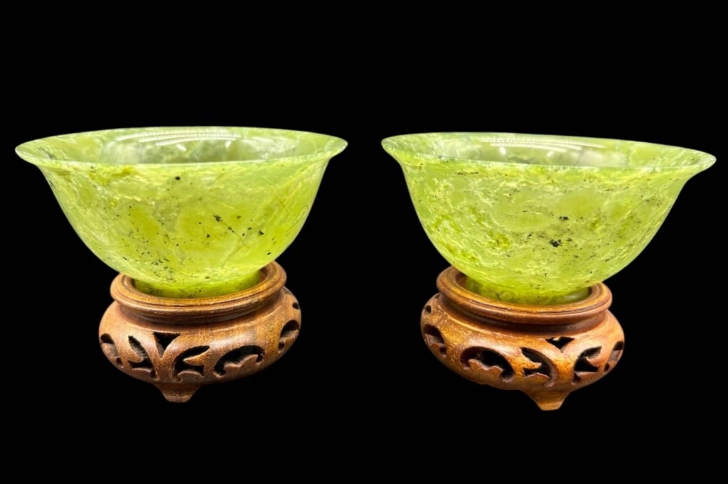 PAIR GREEN HARDSTONE BOWLS ON STANDS 4": Pair of decorative translucent apple-green hardstone bowls, each permanently affixed/glued to a carved hardwood display base. The shallow bowls feature flared rims, polished surfaces and attractive na
