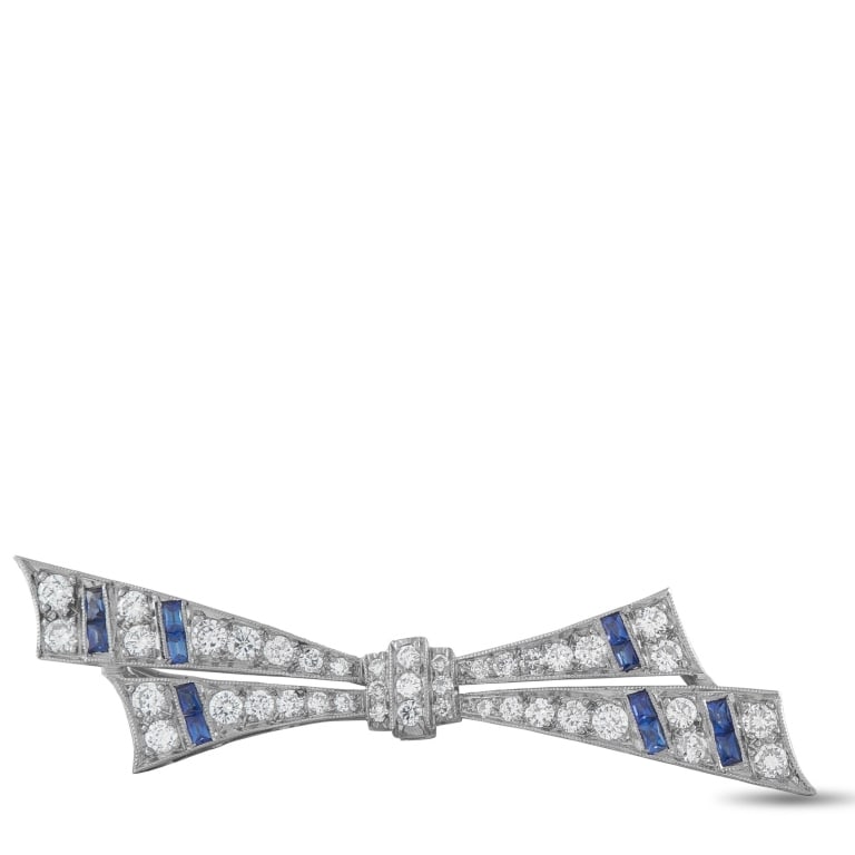PLATINUM 0.90CT DIAMOND AND SAPPHIRE BOW BROOCH: A graceful estate platinum bow brooch in the Art Deco tradition, exquisitely pav-set with round brilliant diamonds totaling 0.90 carats throughout its elegant ribbon form. Calibr-cut blue sapphires ac