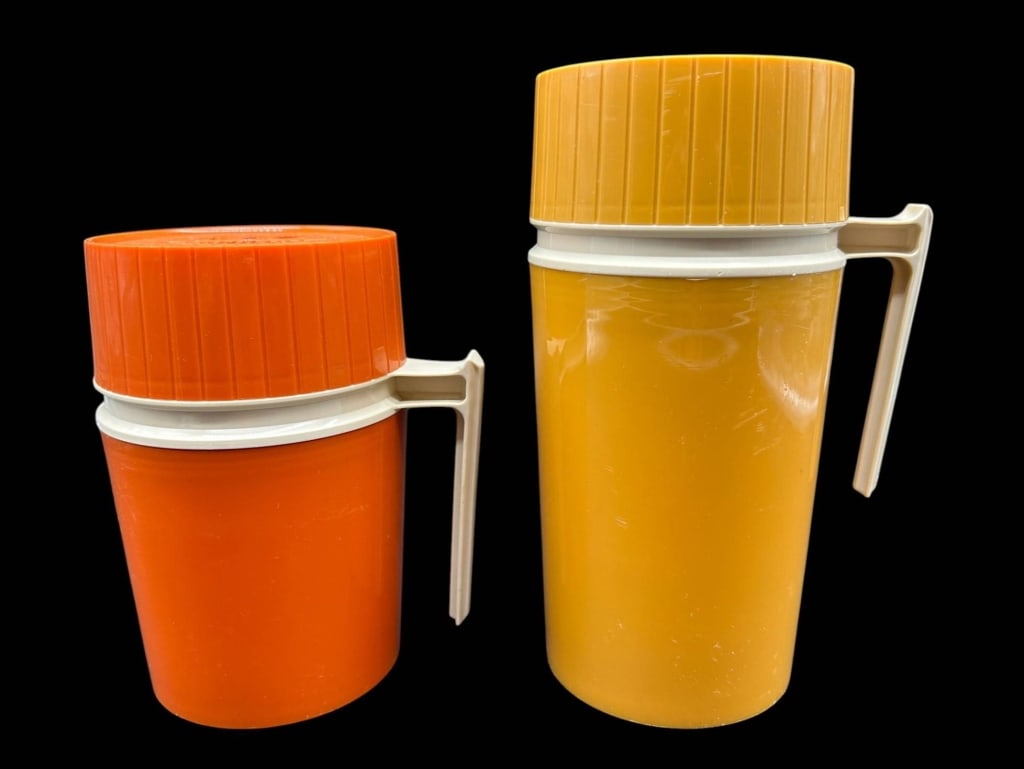 VINTAGE THERMOS VACUUM JARS SET OF 2 8.5": Vintage set of two Thermos vacuum food jars in classic mid-century orange and golden yellow colorways, each with contrasting cream-colored handle and wide ribbed screw-on lid. Both retain molded manuf