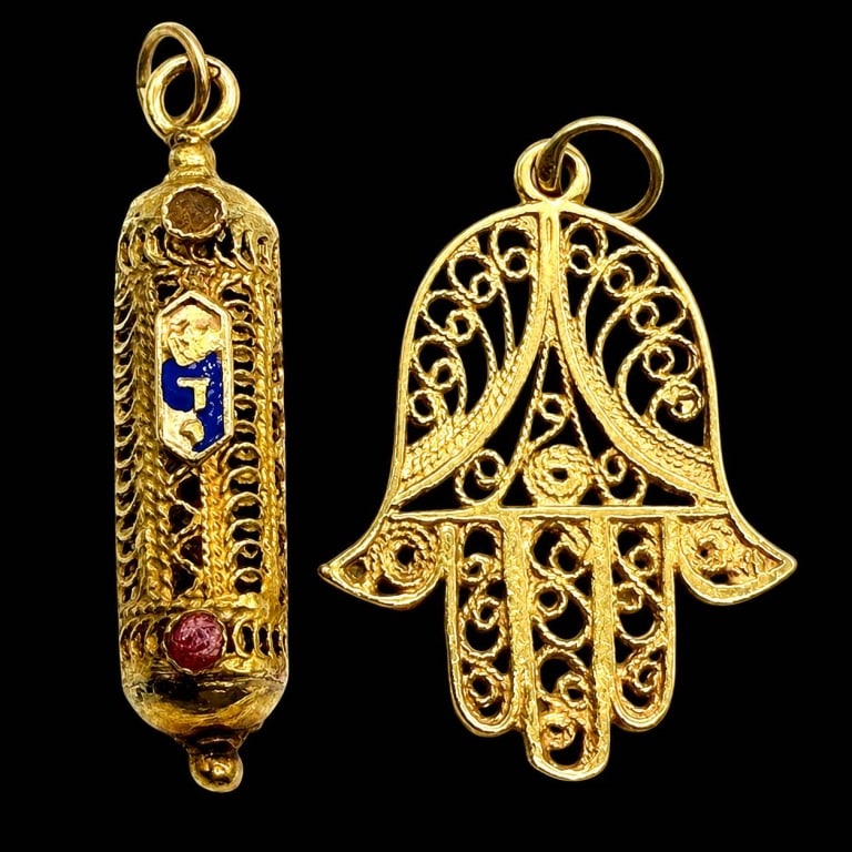 18K GOLD HAMSA AND MEZUZAH PENDANT CHARMS: A finely crafted pair of vintage 18K yellow gold Judaica charms comprising an ornate filigree Hamsa hand and a cylindrical mezuzah pendant. The Hamsa displays intricate openwork scroll decoration and 