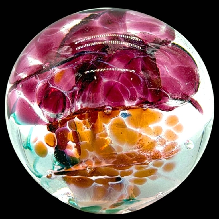 COLORFUL ART GLASS FLORAL PAPERWEIGHT 2": Decorative hand-blown art glass paperweight featuring a vivid dimensional floral composition encased within clear glass. The interior displays rich cranberry, ruby and magenta flower forms accented by