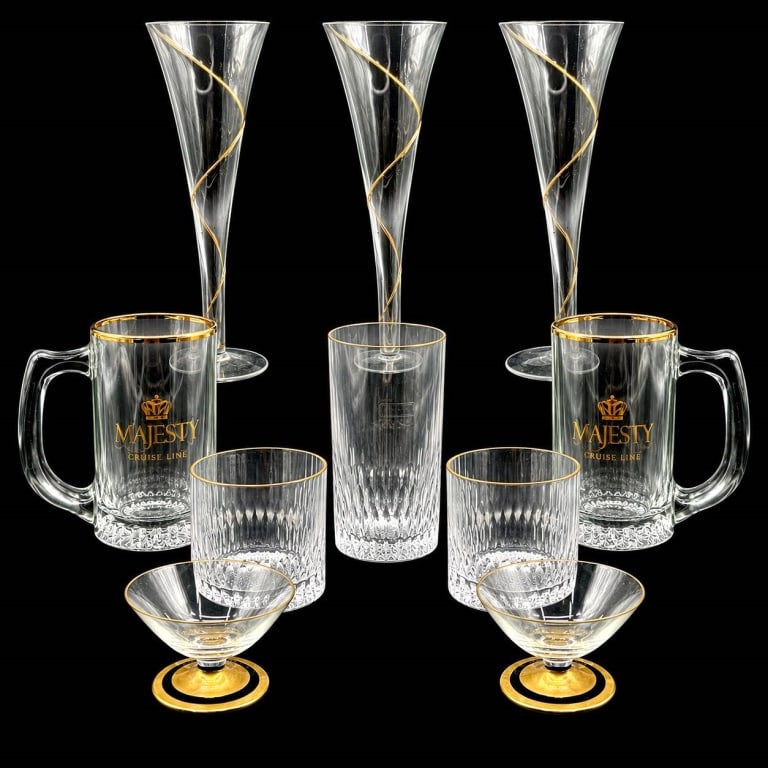 10 PC GOLD RIMMED GLASSES & STEMWARE LOT: Elegant assortment of 10 clear glass pieces in five styles: three tall trumpet-shaped flutes with gold spiral decoration, two handled mugs with gold Majesty Cruise Line lettering and crown emblems, tw