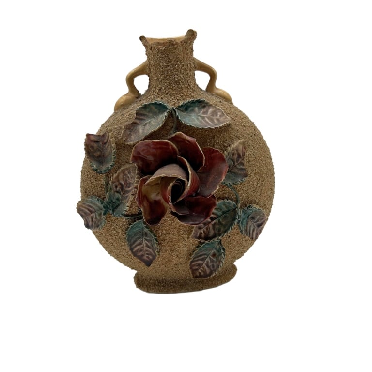 Textured Ceramic Vase with Applied Flower and Leaf: Textured ceramic vase featuring a round body with two small handles near the neck, adorned with applied flower and leaf accents in red and green. Measures approximately 8 inches tall and 7 inches wide