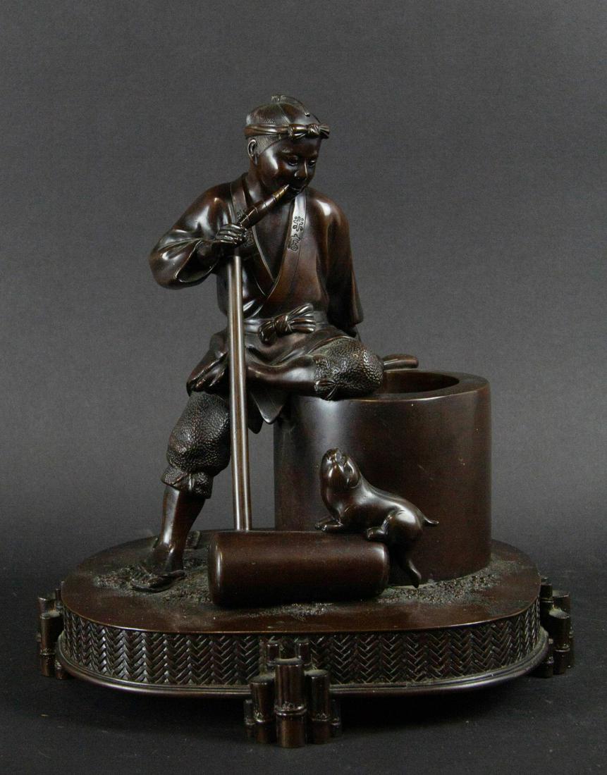 A Meiji Bronze 'Mochitsuki' Figure.: Japanese. Depicting a man and his dog taking a break from pounding rice into mochi. Cartouche to base marking the place of manufacture as a Japanese bronze foundry in Kawabe village in Ehime prefectur
