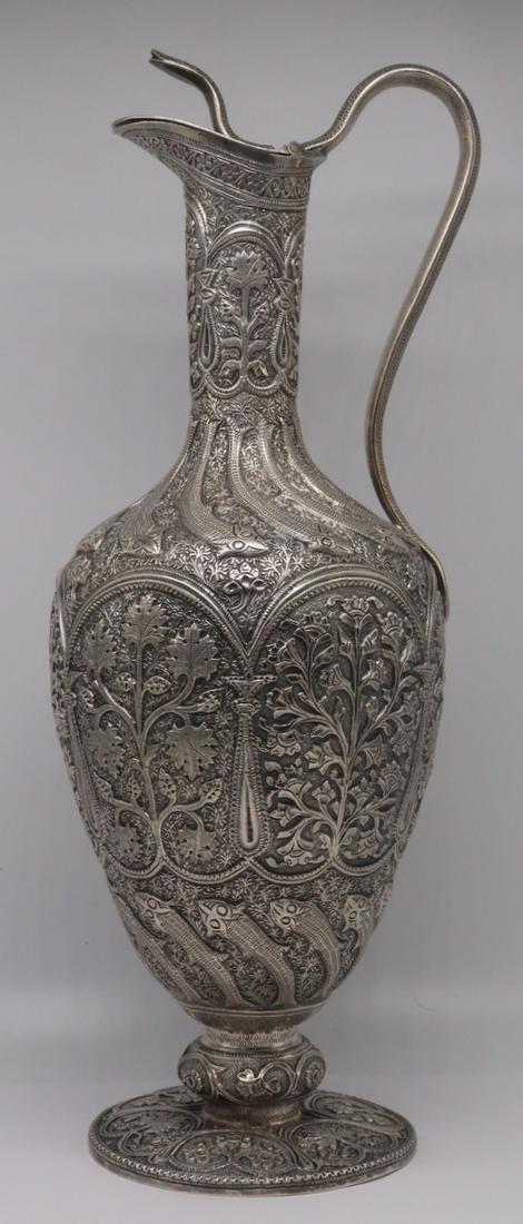 SILVER. Indian Kutch Silver Claret Jug with Snake.: Indian Kutch silver claret jug with snake handle and heavily chased design throughout depicting foliage and fish; atop a pedestal base of foliate decorated frames. Most surely Kutch silver, late 19th 