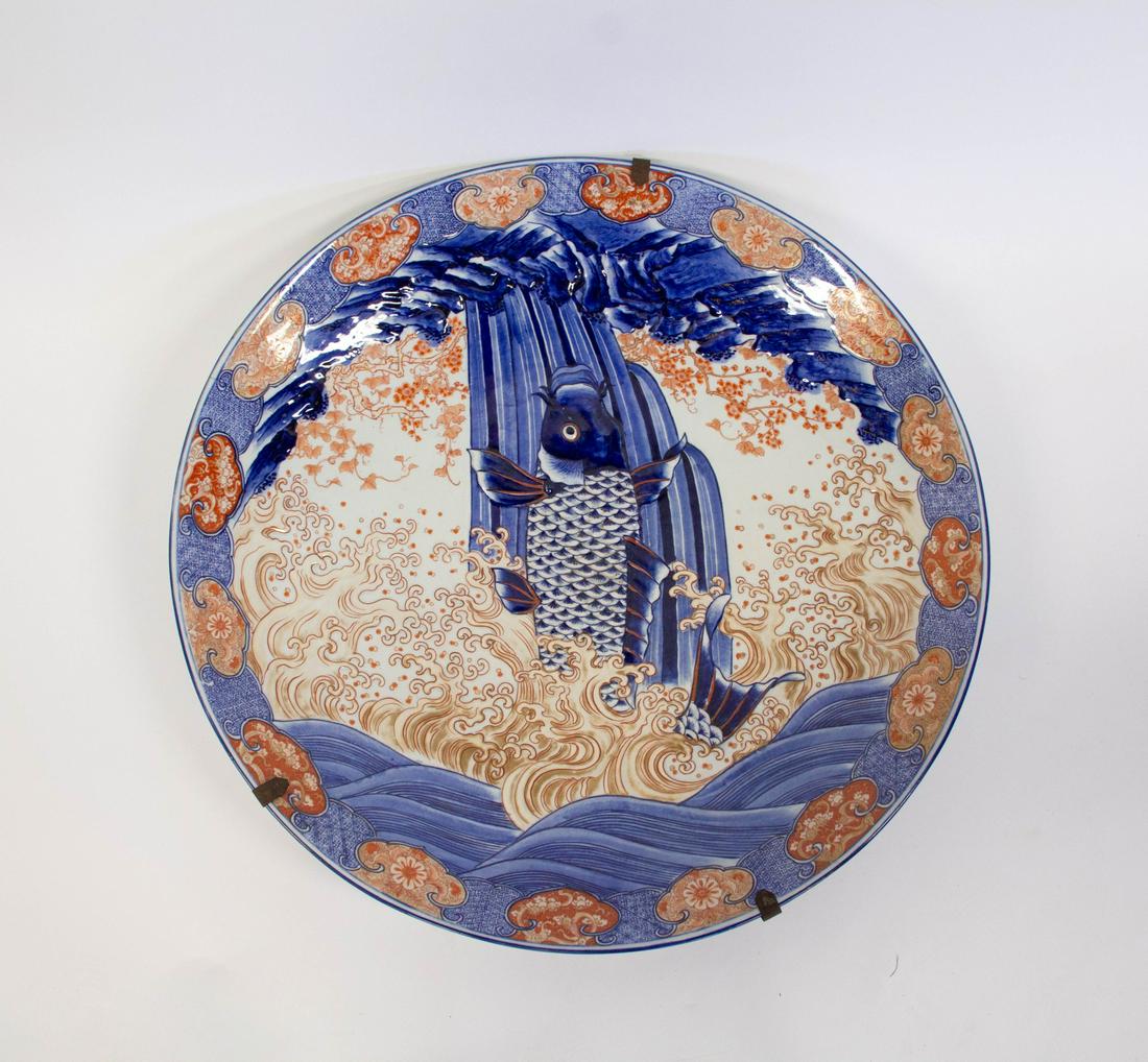 A Massive Meiji "Dragon Gate" Imari Charger.: Japanese, 18th/19th century. Incised and painted with a carp leaping amongst frothy golden waves to a rocky outcropping. Bordered with lappets of delicately painted brocades in blue, red, and gold. Un
