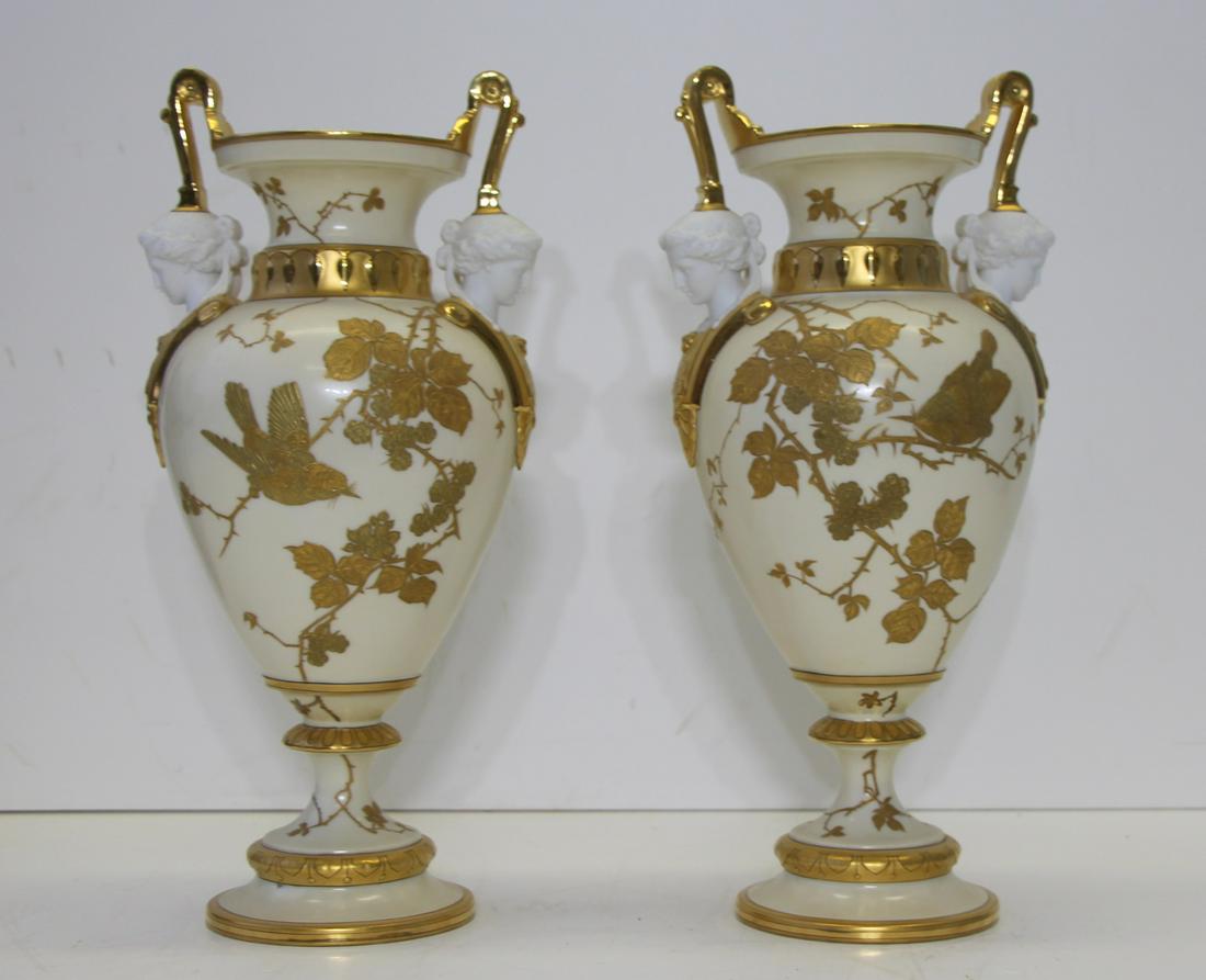 Pair of Gilt Decorated Porcelain Urns.: With Parian heads of beauties to the base of each handle. Apparently unmarked. From a Westchester, NY estate. - Dimensions: : 8" w x 15.25" h.