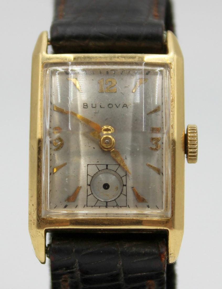 JEWELRY. Men's Bulova 14kt Gold Convex Watch.: A men's Bulova 14kt gold convex watch. This watch by Bulova features a 21mm (excluding crown) 14kt gold convex rectangular watch case, silver tone dial, applied gold tone Arabic numerals and dagger in