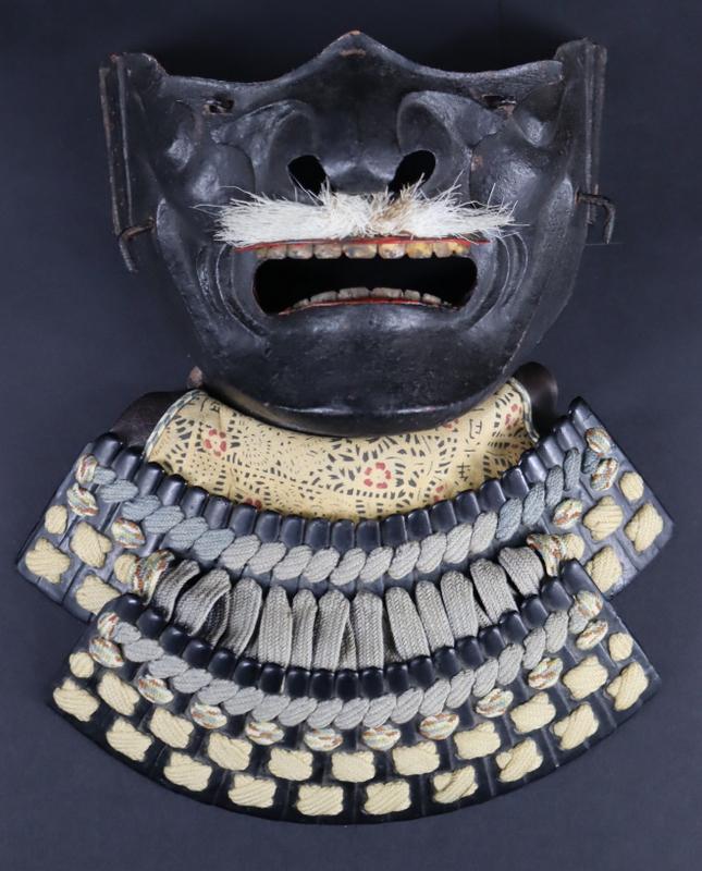 MILITARIA. Japanese Samurai Armour Ressei Menpo: Half Mask. A ressei menpo, complete with removable nose-piece, mustache, (1) plate leather backed fabric yodarekake with lacing, (2) plate yodarekake with lacing, and red interior lacquer. From a Dela