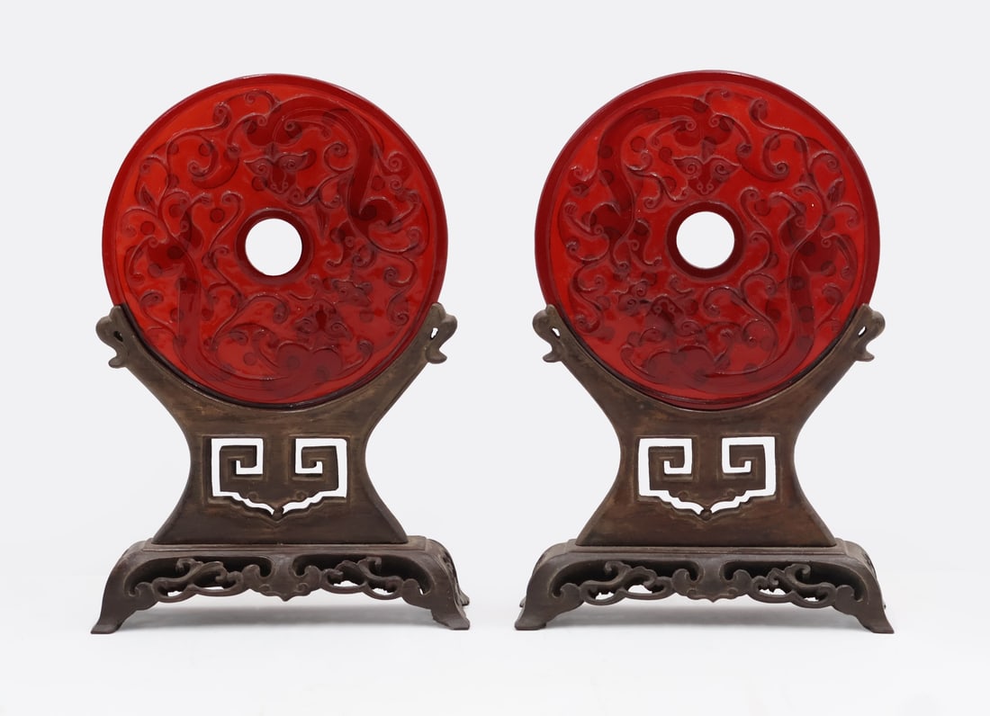 Pair of Peking Glass Discs on Wooden Stands.: Includes a pair of red Peking glass bi discs displaying elongated qilins alongside vegetal motifs to one side with archaic style scrollwork to the verso. Accompanied by two wooden stands. From a Clift