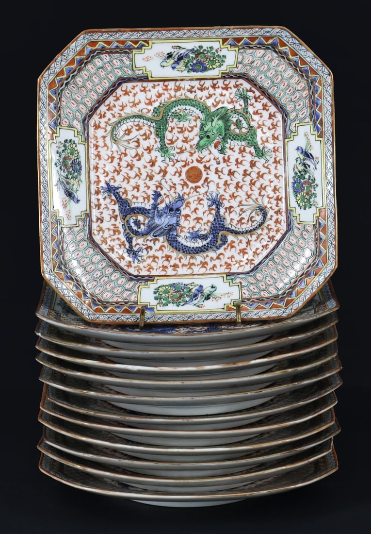 (12) Chinese Enamel Decorated Dragon Plates.: A set of (12) footed square form plates displaying two dragons chasing the flaming pearl surrounded by flames. The outer rims are decorated with registers of geometric patterns and medallions of birds