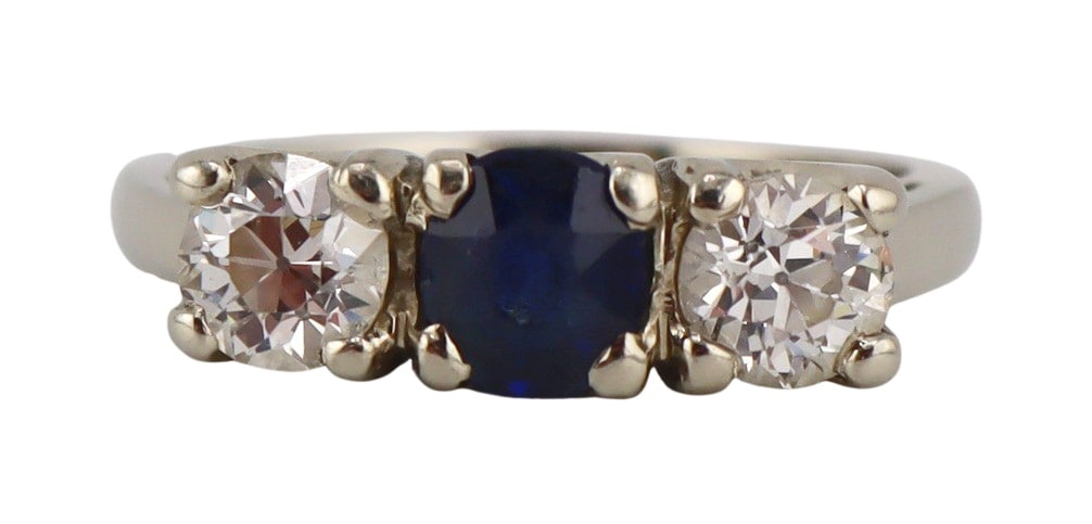 JEWELRY. 13.5kt Gold, Diamond and Sapphire Ring.: 13.5kt white gold ring displaying a central oval faceted sapphire flanked by (2) Old European cut diamonds. Sapphire measures approx. 4.5mm x 5.2mm; diamonds measure approx. 4.4mm each. Apparently unm