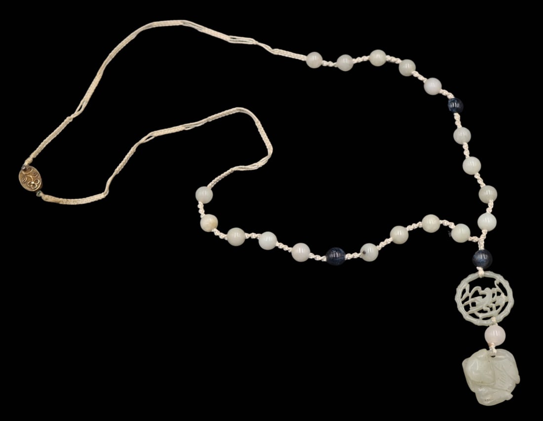 JEWELRY. Carved Celadon Jade Necklace.: Single strand braided necklace displaying (18) celadon jade beads, (3) polished blue stone beads, a circular carved Celadon jade pendant with central bird and bamboo surround, and terminating in a car