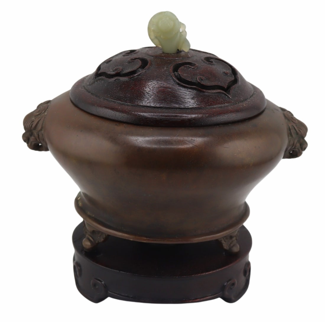 Chinese Bronze Censer with Carved Jade and Wood: Lid. Signed Chinese bronze tripod censer with foo dog handles - signature to the underside. With carved wood lid displaying pierced ruyi pendants and a carved jade finial of a bird to one side and a f