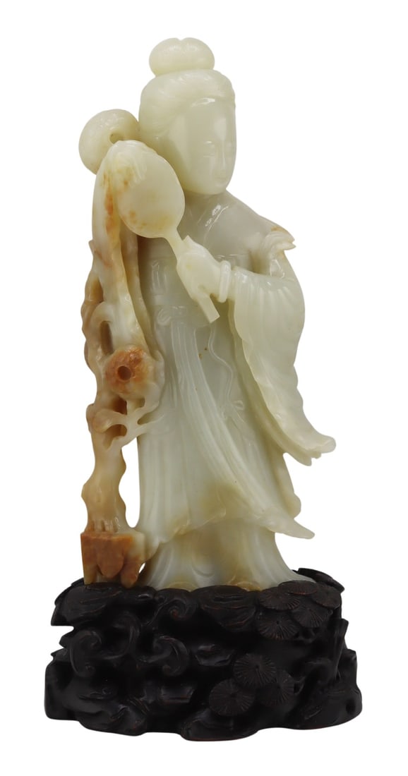 Chinese Carved Jade QuanYin with Base.: Chinese carved standing Celadon jade of a Quanyin holding a fan and standing beside a flowering tree. With russet jade highlights, and set atop a fitted carved wood base displaying rocks and pine tree