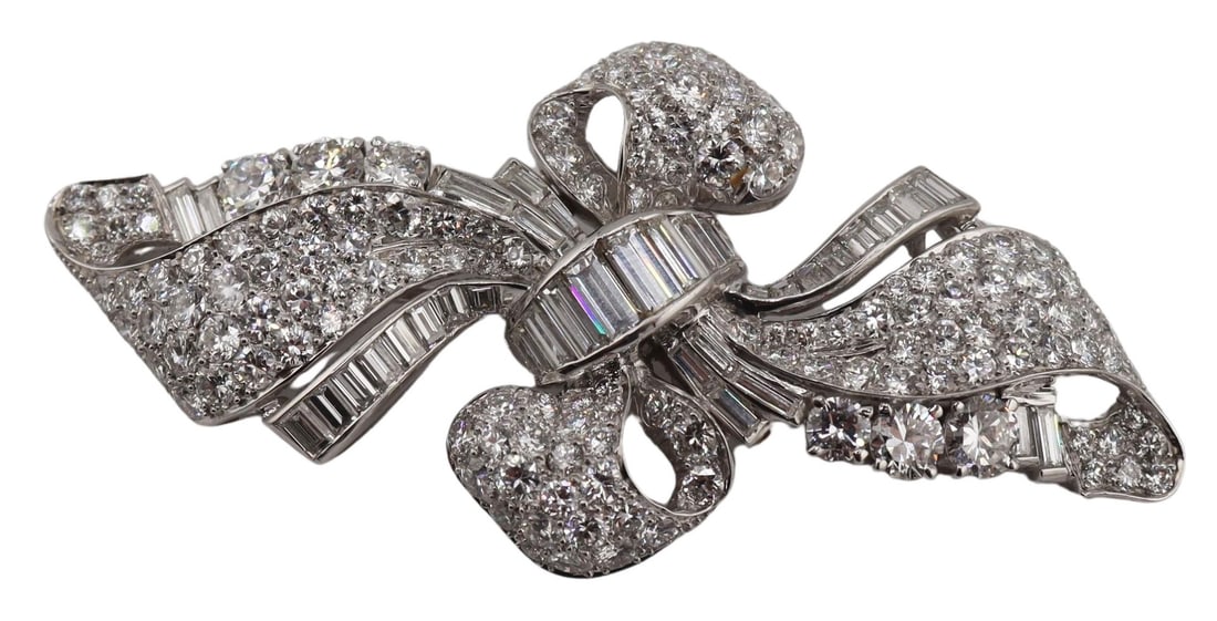 JEWELRY. Platinum and Diamond Pendant or Brooch.: Art Deco bow or ribbon form platinum brooch or pendant accented by an array of diamond baguettes and round full cut diamonds. The (2) largest diamonds measure approx. 3.5mm each. The underside display
