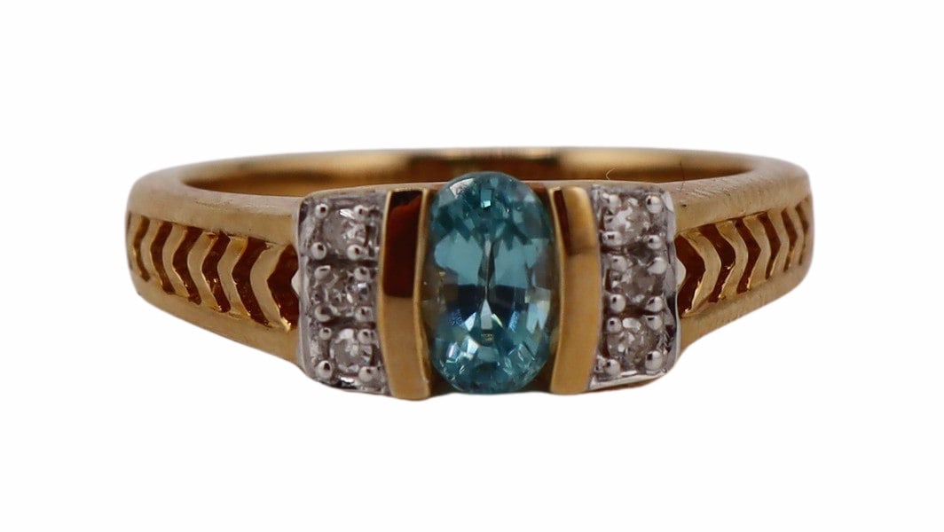 JEWELRY. 14kt Gold, Blue Zircon, and Diamond: Ring. 14kt yellow gold ring displaying a central 0.70ct oval faceted blue Zircon accented by (6) round faceted diamonds and displaying a pierced chevron pattern to the shoulders of the shank. Total ap
