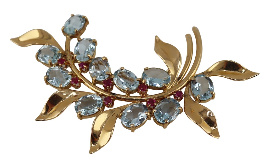 JEWELRY. 14kt Gold, Ruby and Blue Gem Brooch.: Vintage/retro 14kt yellow gold foliate form brooch displaying (11) prong-set oval faceted blue gems, presumably Aquamarines, accented by (8) prong-set round faceted rubies and dispersed amongst leaves