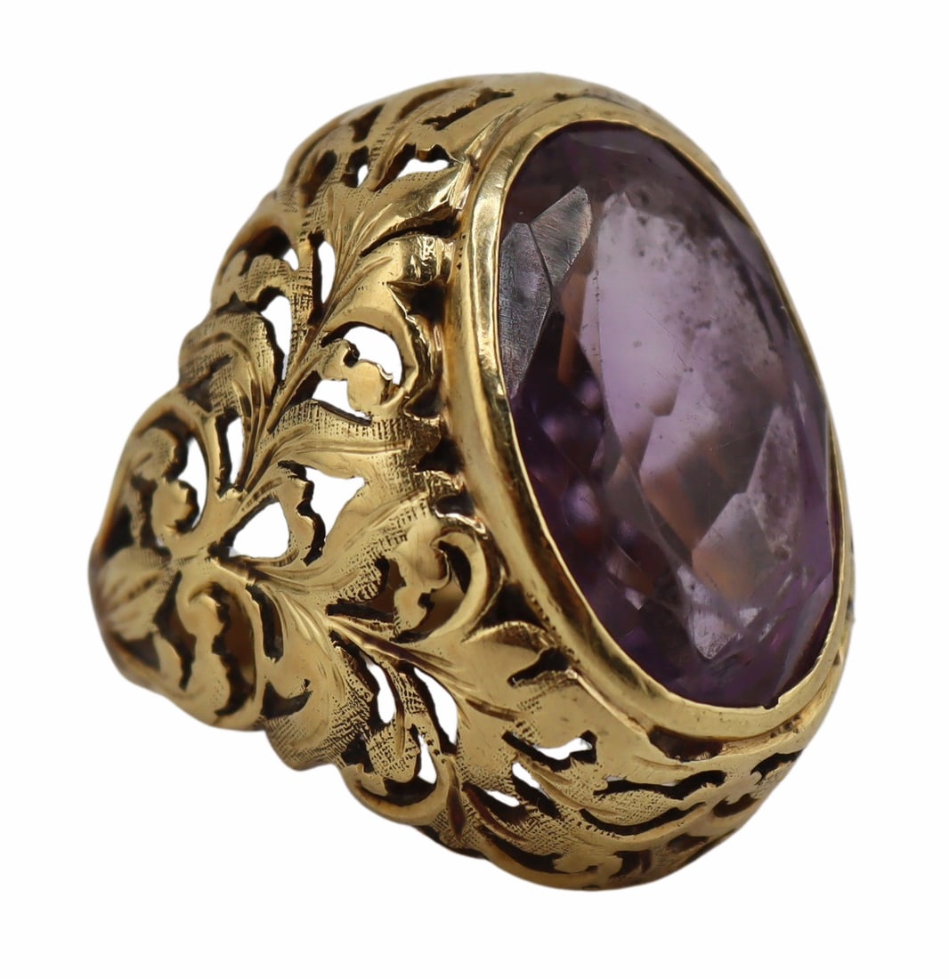 JEWELRY. 18kt Gold and Amethyst Scroll Motif Ring.: 18kt yellow gold cocktail ring displaying a central bezel set oval faceted amethyst set within a pierced scroll motif surround and tapered band. Amethyst measures approx. 12.5mm x 18.5mm. Total