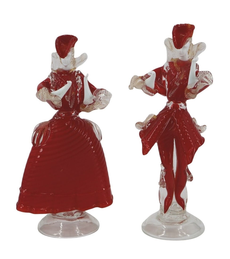 A Pair of Red Venetian Glass Figures: Two ornate Venetian glass figures, a man and a woman, in ornate costumes. With white glass faces and hands, gold flecked costume detail, and overall red color. - Dimensions: 13" tall
