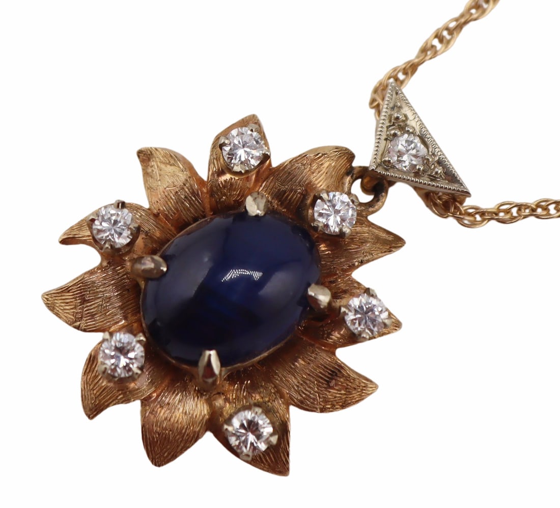 JEWELRY. 13.5kt Sapphire Cabochon and Diamond: Pendant. 13.5kt yellow gold floral form pendant displaying a central prong-set oval sapphire cabochon surrounded by (6) round full cut diamonds. Sapphire measures approx. 7.0mm x 9.0mm. Suspended from