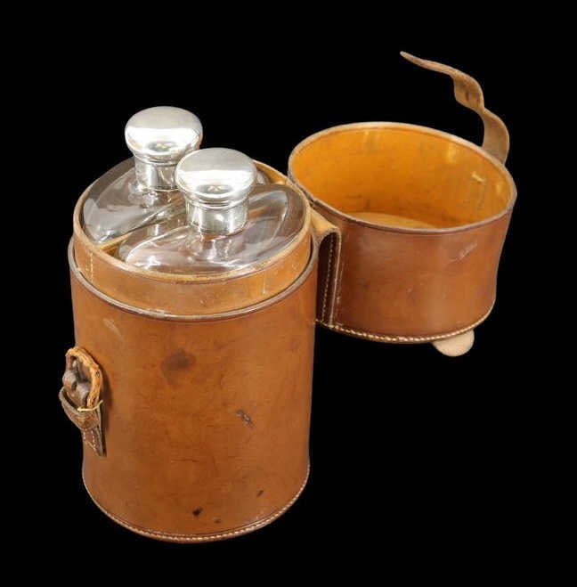 SILVER English Leather Cased Travelling Drinks Set: A handsome leather cased travelling drinks set, housed in a cylindrical brown leather case fitted with a handle and strap with buckle closure. The case opens to reveal a neatly appointed interior, ret