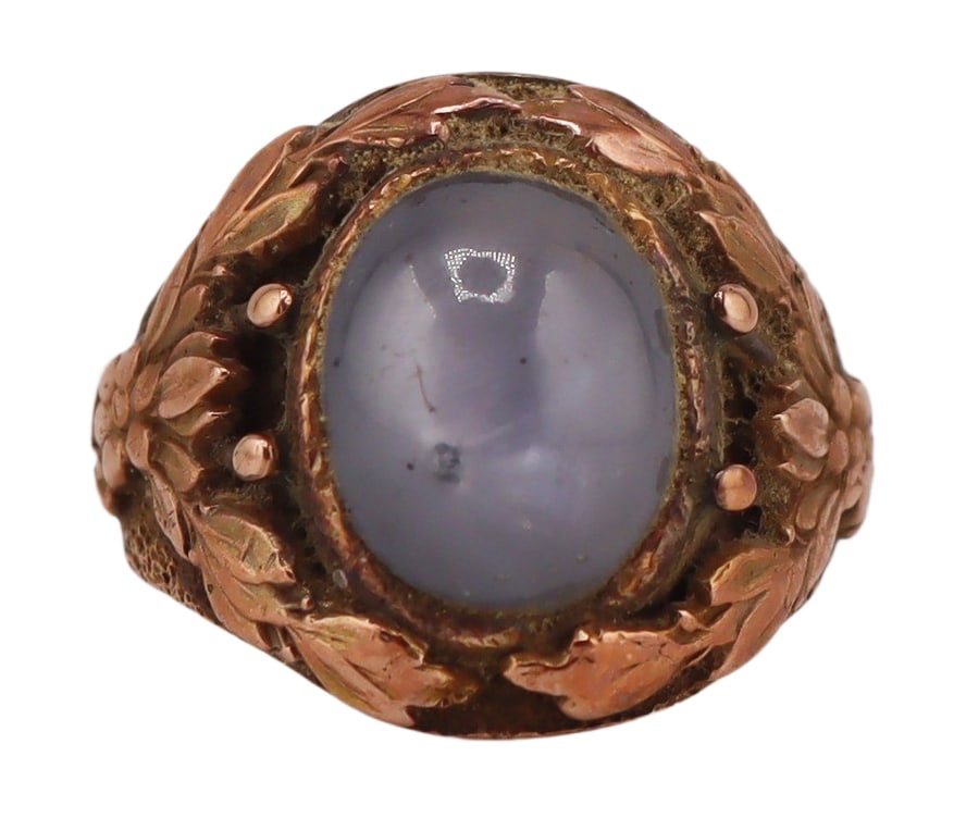 JEWELRY. 14kt Gold and Star Sapphire Ring.: 14kt yellow gold ring displaying a central bezel set oval cabochon blue-grey star sapphire surrounded by applied floral garland. Gem cabochon measures approx. 10.0mm x 8.0mm. Stamped, "14K". Ring size